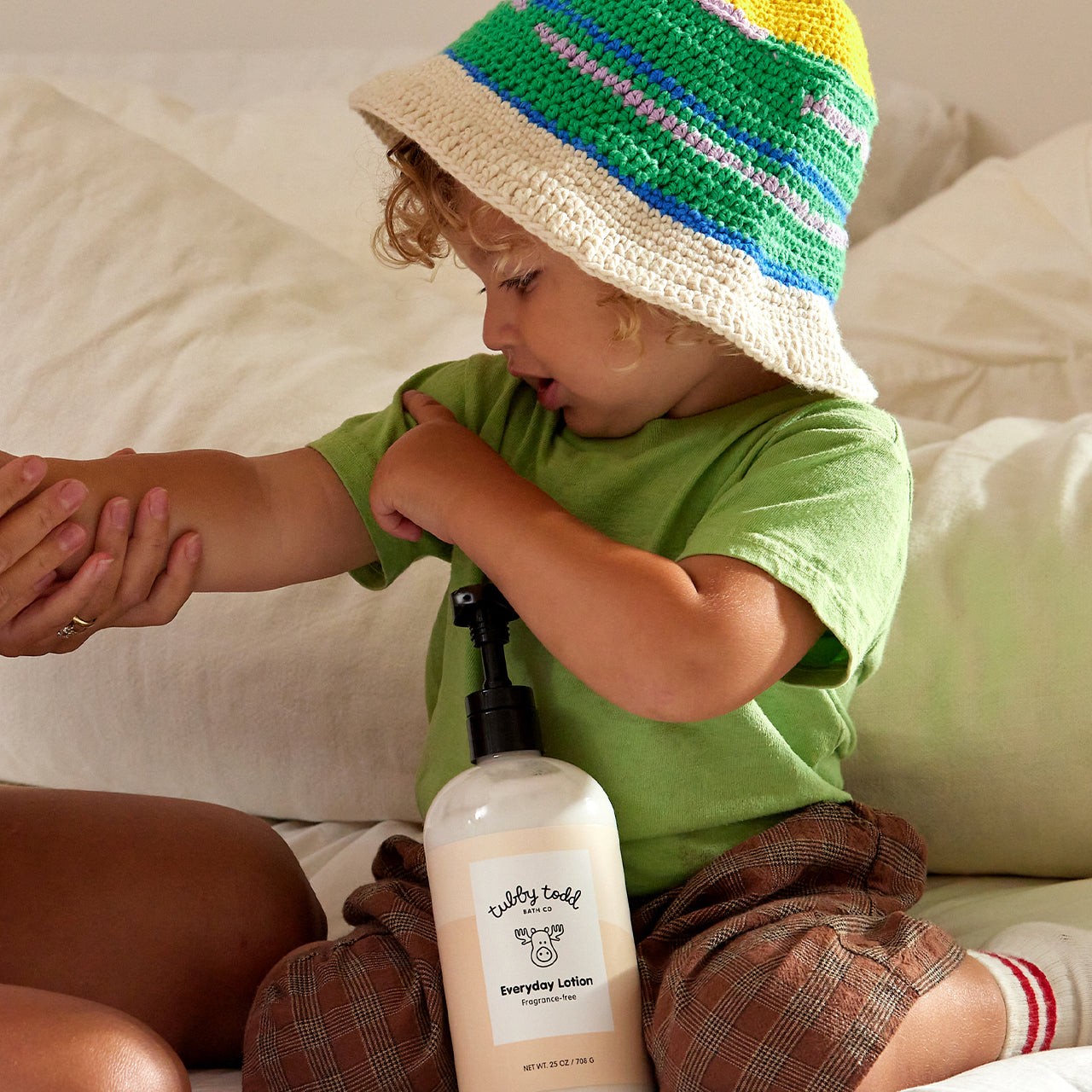 Mom applying the Fragrance-free Everyday Lotion on her baby boy's arm on the bed.